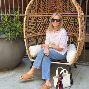 Woman seated in outdoor chair wearing a cropped shirt and jeans.
