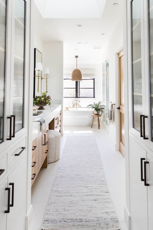 Love this beautiful bathroom with a woven light fixture, wood vanity cabinets, and white linen cabinets